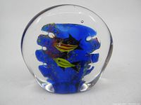 Front angle of first handblown glass paperweight showing yellow and black fish inside blue aquarium-like background.
