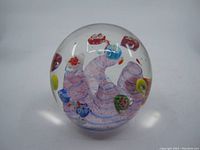 Front view of the spherical glass paperweight showing clear glass with pink and red internal swirls and colorful floral decorations.