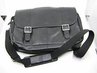 Front view of black leather messenger laptop briefcase with double buckle flap and adjustable shoulder strap laid out.