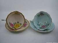 Top view of two Old Paragon teacups and saucers, one blue and one cream-colored, both with floral design and gold trim.