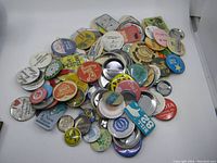 Overview of a large assortment of pinback buttons piled together showing various sizes, colors, and worn conditions.