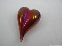 Heart-shaped red iridescent glass paperweight angled to show full shape and iridescent color.
