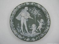 Full view of green jasperware porcelain plate with central lute player and cherubs scene, surrounded by floral border.