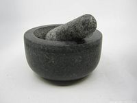Side view showing the full stone mortar and pestle set with smooth rounded shape and visible wear marks.