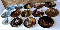 Photo showing all 14 collector plates arranged on a surface, primarily Norman Rockwell artwork.