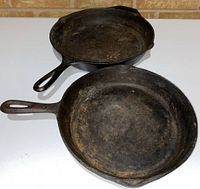 Two cast iron skillets shown from above, showing wear and rust on surfaces.