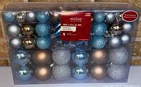 Clear view of the box showing multiple rows of blue and silver spherical ornaments with matte, shiny, and glitter finishes.