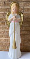 Front-facing image of vintage angel blow mold figure with golden wings, white robe, pink belt, holding golden horn, showing paint wear and aged appearance.