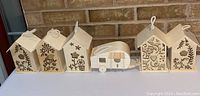 All six wooden craft items arranged in a row showing various house shapes and a camper trailer, all unpainted with laser-cut floral and botanical designs.