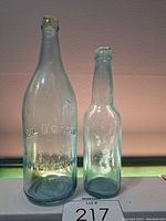 Two vintage glass bottles displayed side by side on a white surface under light.