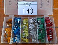 Top view of plastic storage case with seven compartments holding automotive blade fuses sorted by color.