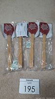 Photo showing 4 brand new Pampered Chef Holiday Spatulas still in packaging. Each spatula has a wooden handle and red silicone head with 'Baking Spirits Bright' text.