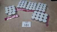 Photo showing five packages of small craft containers arranged on carpet. Four packages each contain 12 containers, one package has 11 containers. Containers are clear with white lids.