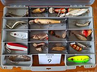 Top view of a tackle storage box filled with approximately 19 vintage lures in separate compartments.
