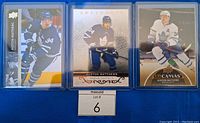 Three Auston Matthews hockey cards in top loaders laid side by side on blue background.