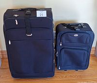 Photo of two black fabric suitcases, a large one and a smaller one, standing side by side on a hardwood floor.