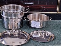 Two stainless steel pasta inserts and one large spare lid shown together on surface, highlighting size differences and polished finish.