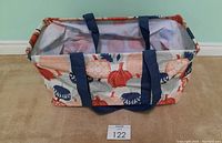 Photo of large rectangular utility tote with fall pumpkin pattern, navy straps, open top showing interior lining and wire structure.