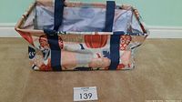 Photo of rectangular tote bag with fall pumpkin and leaf print, navy handles, inside lined with light fabric, wire frame maintains structure.