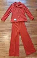 Full view of the orange leisure suit top and pants laid flat on wooden floor