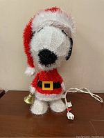 Front view of Snoopy figure dressed in Santa outfit, LED lit, with power cord and bell visible.