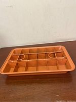 Copper metal brownie pan with 24 square compartments formed by grid dividers, placed on wooden surface photographed from a front angle.