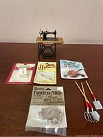 Photo showing all items: miniature sewing machine, packaged scissors, miniature chains bag, mini potholder kit, and four miniature gardening tools.