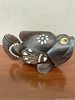 Side view of hand carved ebony wood fish sculpture showing mother of pearl inlays on fins, tail, and body, with shell eyes.