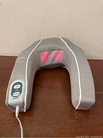 Gray U-shaped neck massager device with visible red glow from massage nodes, wired control attached.