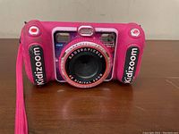 Front view of pink VTech Kidizoom Duo DX kids camera showing dual lens, flash, and wrist strap.