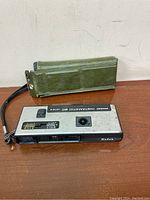 The Kodak Pocket Instamatic 60 camera with the green carrying case placed upright behind it.