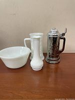 Three milk glass items and one metal stein shown on wooden surface against plain background.