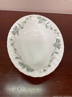 Top view of white oval serving dish with green leaf and white flower decorative pattern and gold rim.