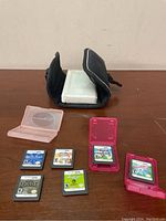 White Nintendo DS console in black carrying case with six DS game cartridges and two pink game card holders on a wooden table.
