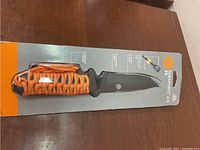 Overall package of the UST ParaKnife 4.0 FS showing orange paracord wrapped handle and protective sheath.