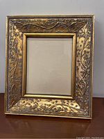 Full view of the rectangular gold-colored decorative picture frame showing detailed leaf and vine motif on the border.