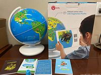 Photo showing globe on white stand, original box behind, four educational cards, and blue kiosk piece in front