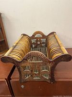 Side angle view showing curved bamboo frame, wood end panels with carved decorative cutouts, and bamboo rods for magazine holding.