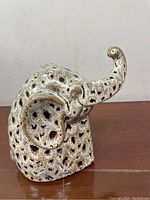 Front and side angle of vintage ceramic elephant with trunk raised, showing speckled black and off-white pattern and textured holes.