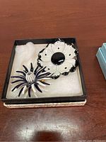 Two vintage costume jewelry floral brooches: one black and white with metal and enamel, the other pink with green enamel leaves.