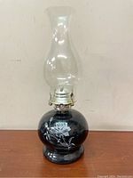 Full view of vintage hurricane oil lamp showing black glass base with white rose floral design and clear glass chimney.