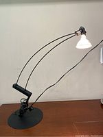 Side angle view of vintage black desk lamp with dual thin metal arms and round base, lamp lit with white conical shade.