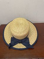 Full side view of vintage Laura Ashley straw boater hat showing natural straw texture and black grosgrain ribbon around brim with bow.