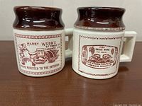 Front view of two ceramic crock coffee mugs with brown glazed rims, square handles, and printed vintage Canadian advertisements.
