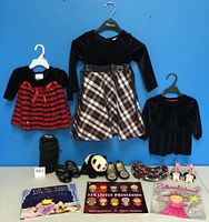 Photo showing three girls dresses hanging and various shoes, books, panties, panda stuffed toy, and baby bottle holder placed in front.
