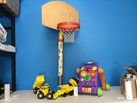 Children's basketball stand next to toy trucks and a colorful walker aid against a blue wall.