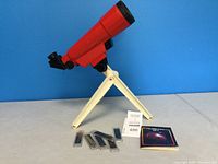 Red Fisher-Price toy telescope with white tripod stand, four slides, and booklet placed in front against a blue background.