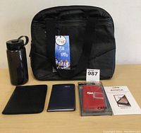 Front view of black Golla laptop bag, water bottle, ID passport holder, agenda, iPhone 6 case, and screen protector on white surface.