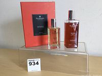 Two Pecksniff's England men's grooming bottles (eau de toilette cologne and shower gel) with original red packaging box on clear stand.