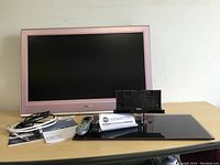 Pink Sony Bravia LCD TV with cables, manuals, remote controls, and stand arranged on a table